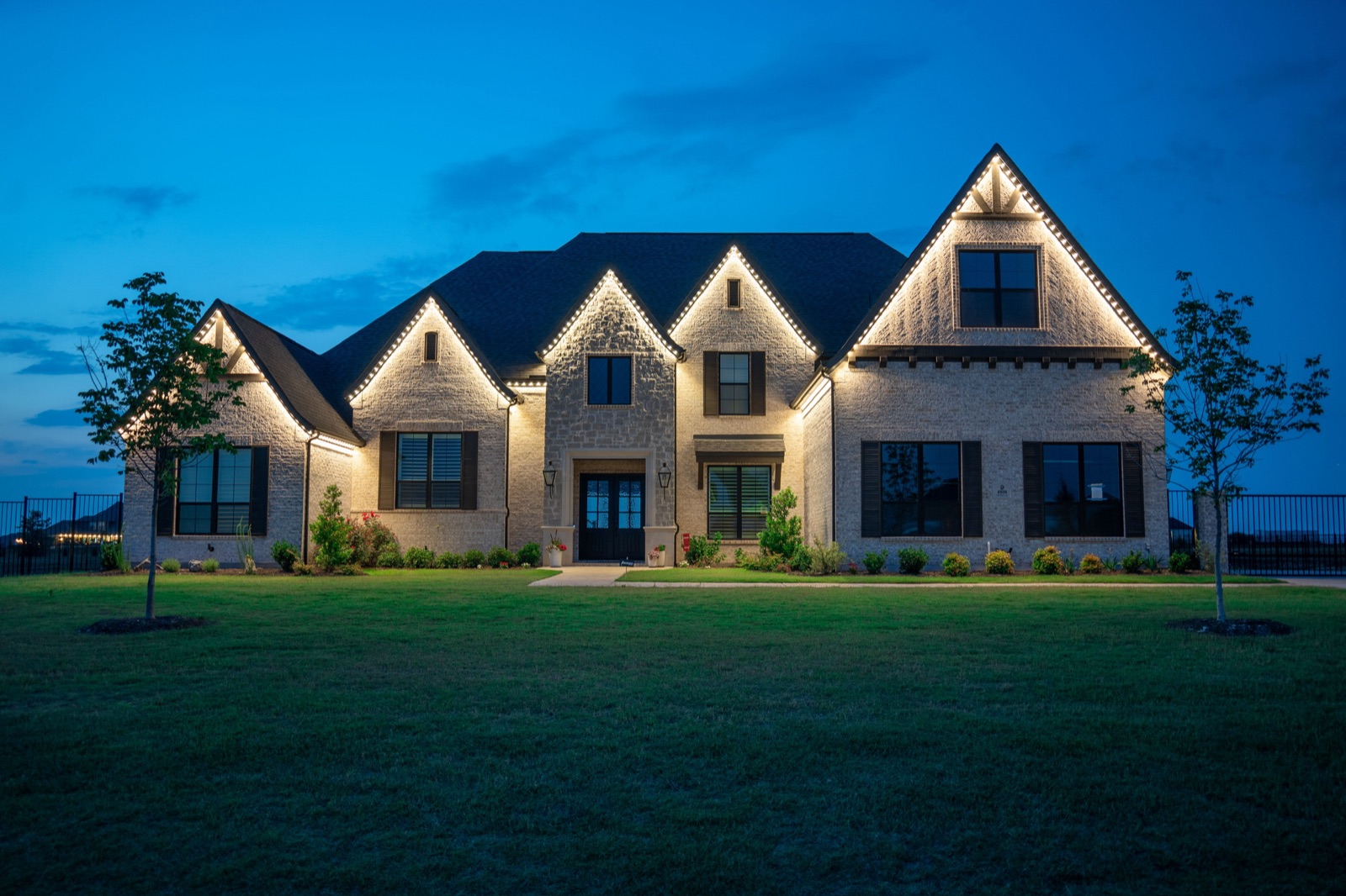 Stone home with warm white permanent roofline lighting at night